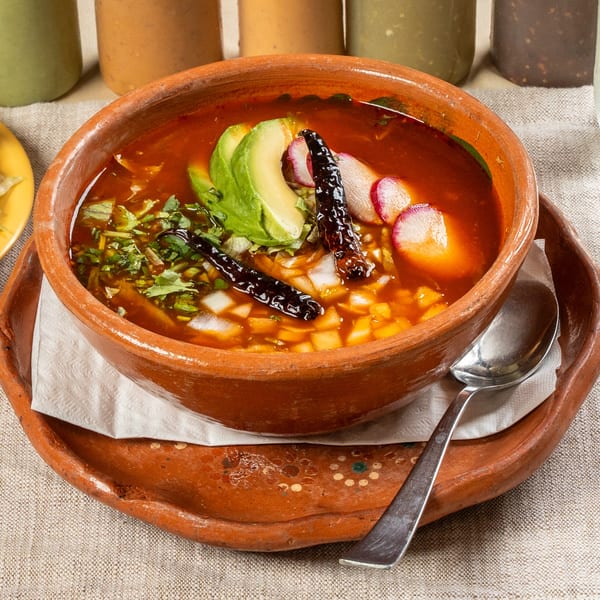 Chavela's Mexican Cuisine pozole in a clay bowl, garnished with avocado, radishes, and dried chilies.