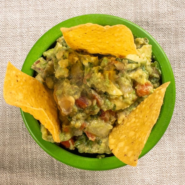 Chavela's fresh guacamole in a green bowl with three tortilla chips, viewed from above.
