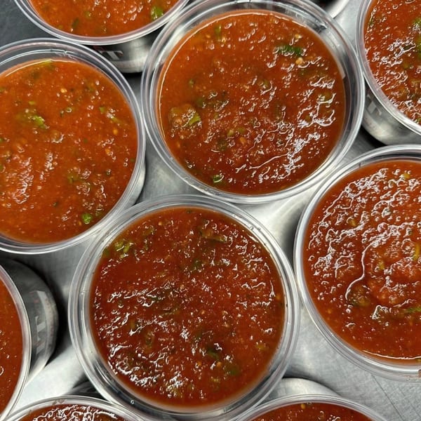 Multiple clear plastic containers filled with vibrant red Chavela's Mexican salsa, ready for takeout.