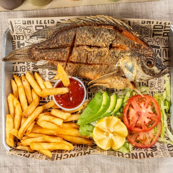 Fried whole fish with french fries, ketchup, avocado, tomato, lettuce, and lemon on a tray.