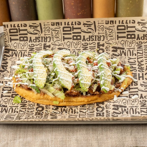 A Chavela's Mexican Cuisine huarache, topped with avocado, lettuce, cheese, and crema, on branded paper.