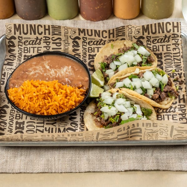 Three Chavela's Mexican Cuisine tacos with rice and beans, garnished with lime wedges.